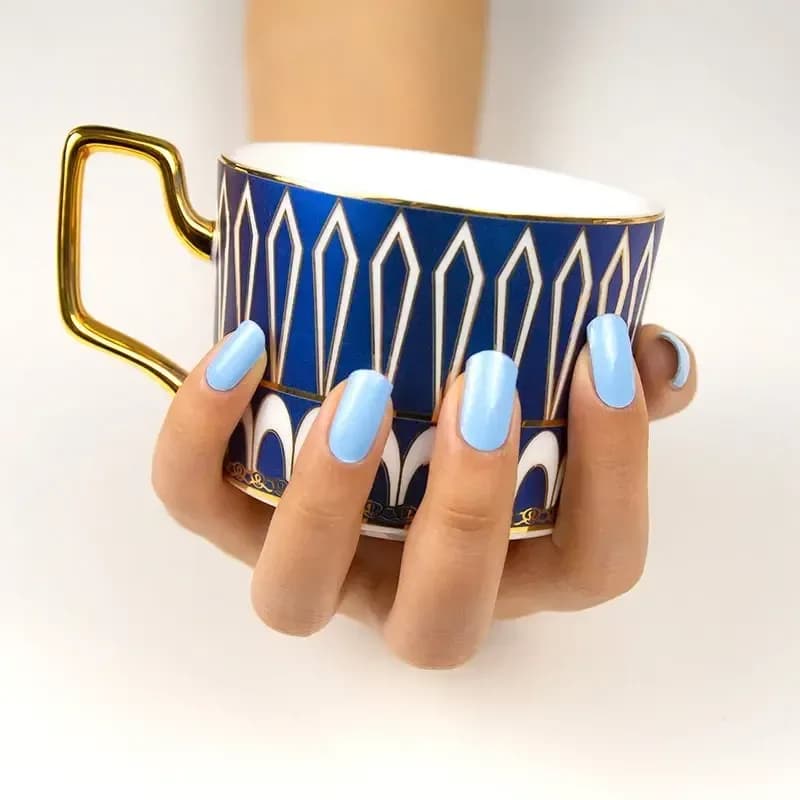 Cloud Nine sky blue manicure holding a blue and gold patterned cup