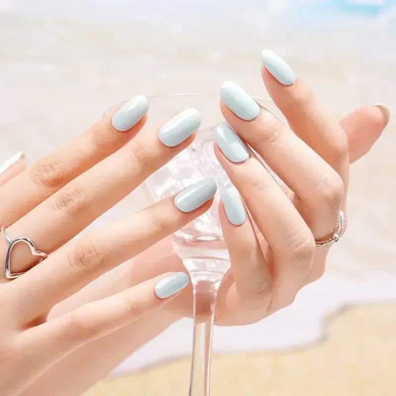 Coastal Breeze pale blue manicure holding a glass by the sea