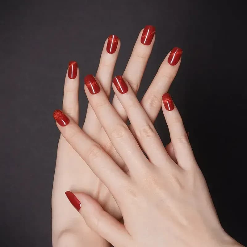 Ruby Slippers glittering ruby red gel nails on crossed hands against a dark background
