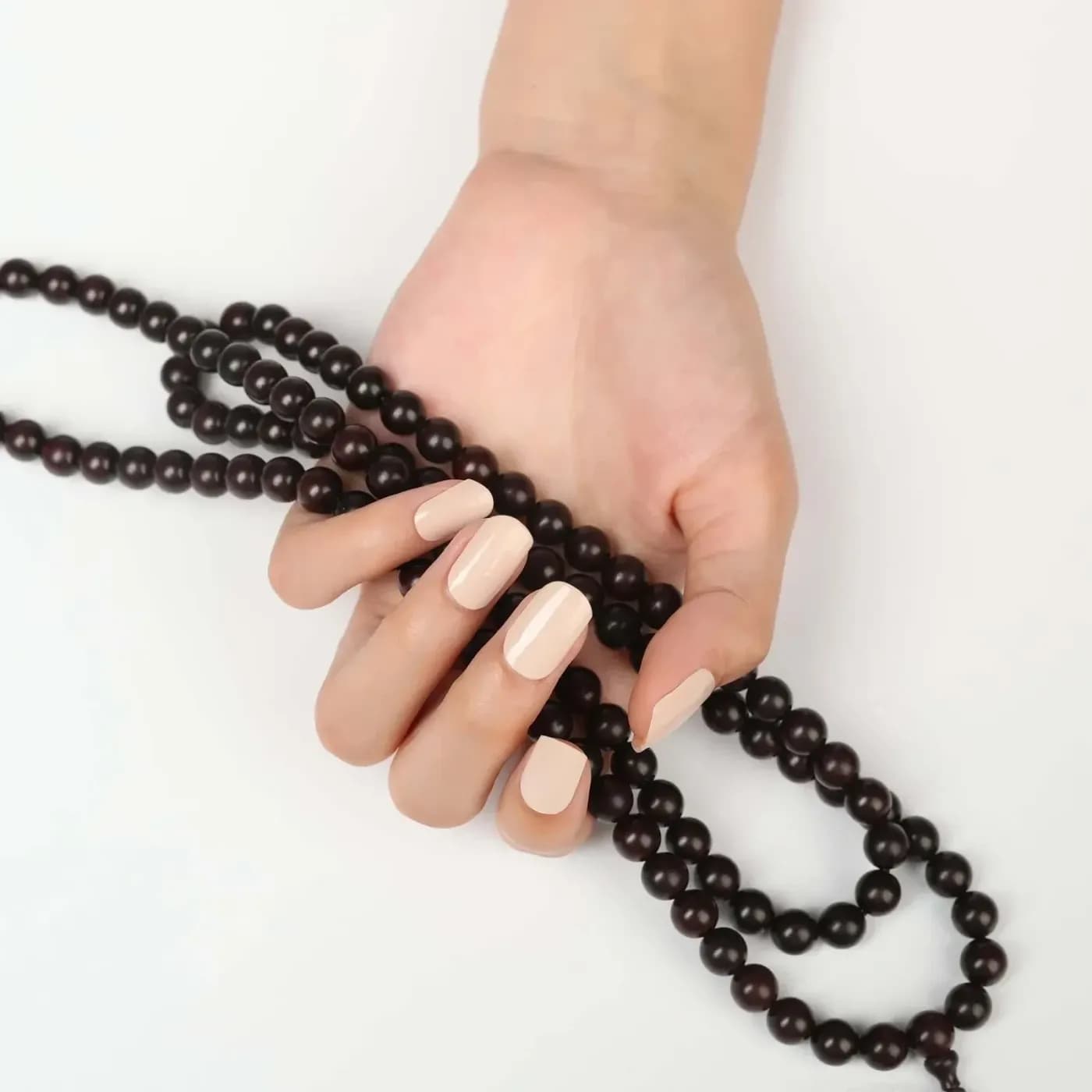 Think Pink pale blush pink gel nails holding a string of dark wooden beads