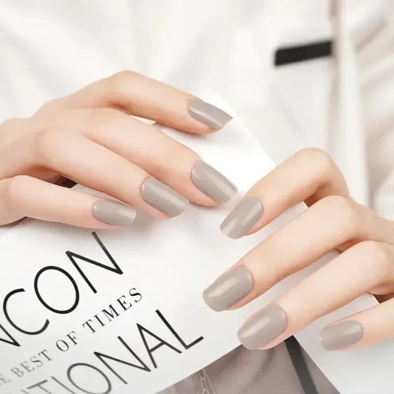 Timeless Taupe greige gel nails on both hands holding a magazine