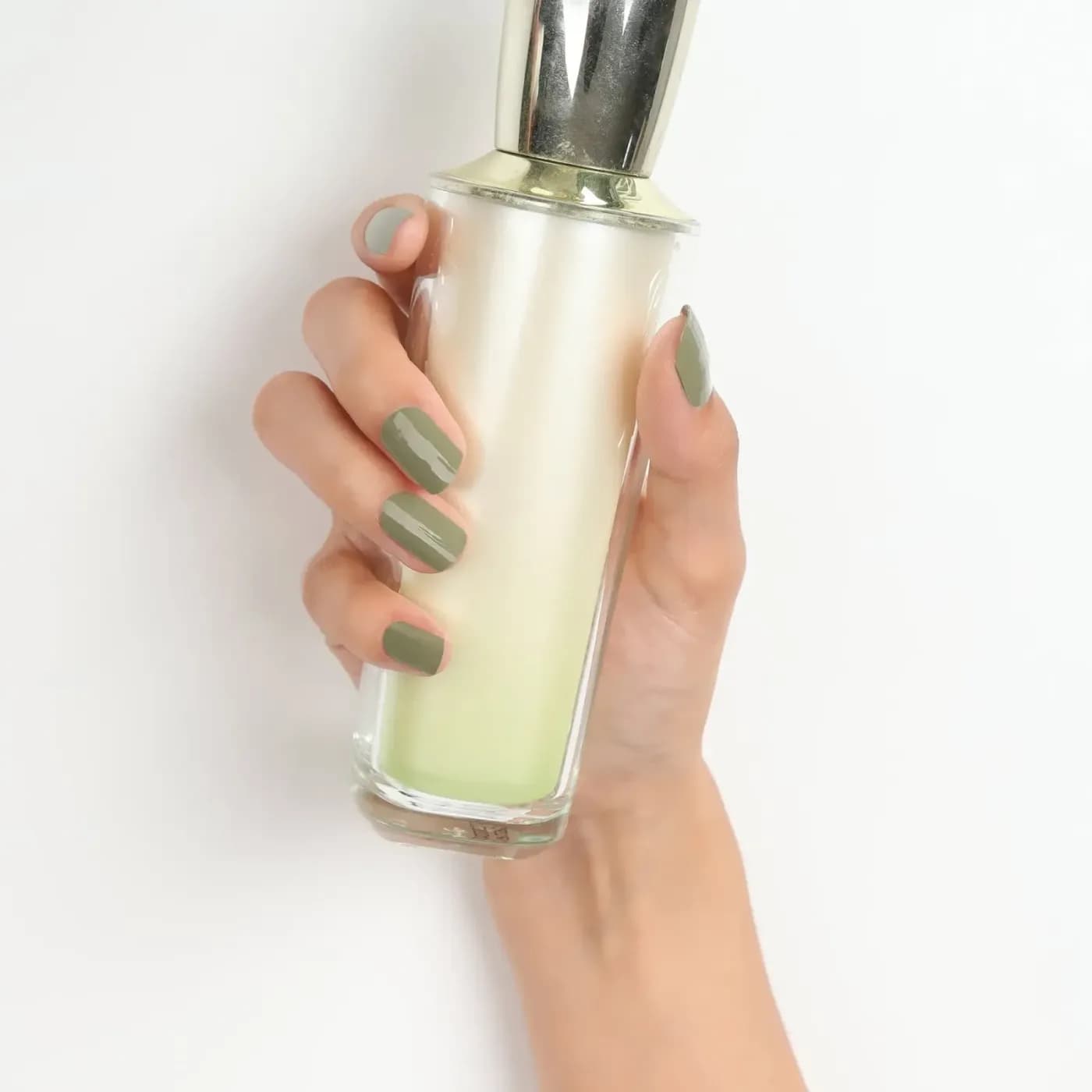 Glossy Urban Jungle sage green gel nails, close up holding a glass bottle