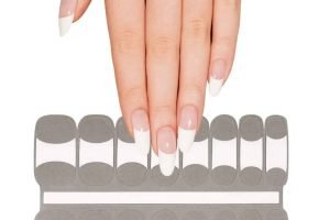 Hand applying French tip gel nail wraps with semi-cured adhesive strips