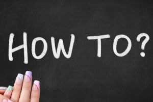 Chalkboard with the words “How To?” written in white chalk, with a close-up of a hand showing pastel-coloured gel nail strips in the corner.