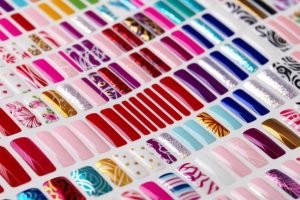 A variety of colourful semi-cured gel nail strips arranged in rows, showcasing different designs including florals, glitter, metallics, and solid colours on a white background.