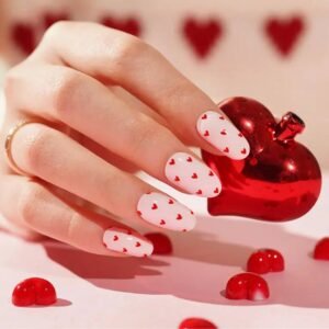 Close-up of Velvora Love Hearts nails: soft-pink base covered in tiny red hearts, holding a red heart prop.